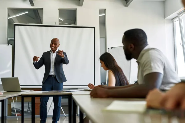 Smiling black male trainer point with finger at trainee during a therapy training session. Multiracial people at open space office.